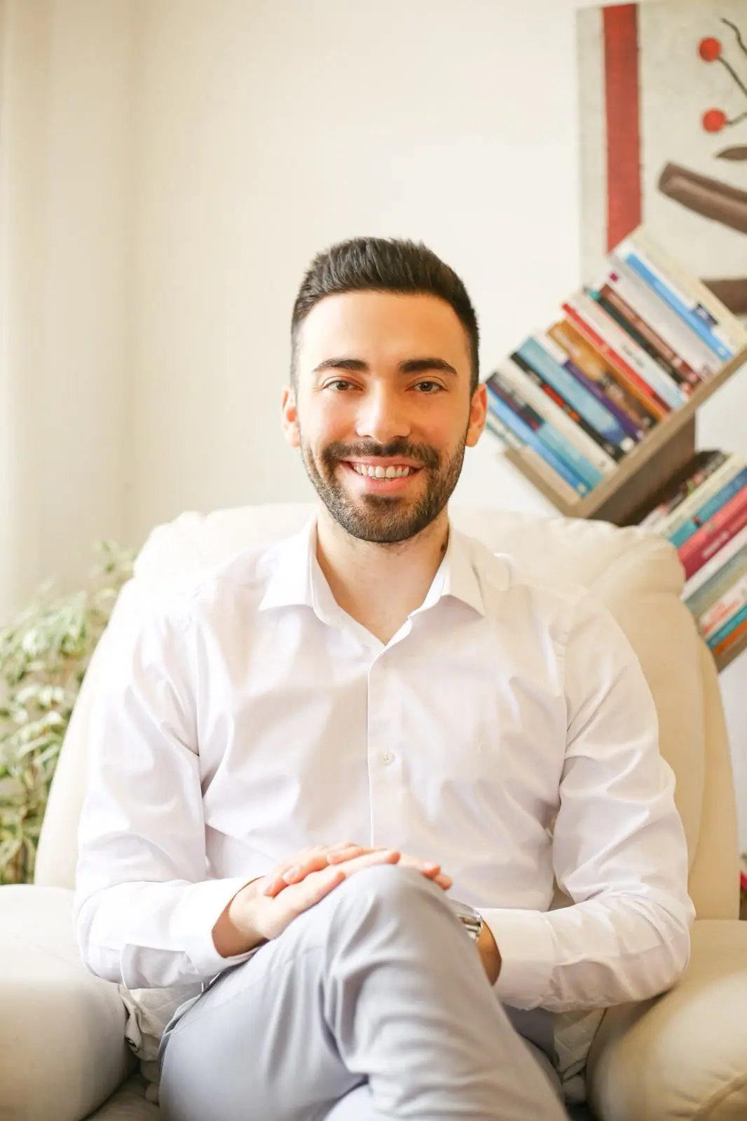 Abdullah Yusuf Kılıç, kitaplık önündeki krem rengi koltukta oturuyor