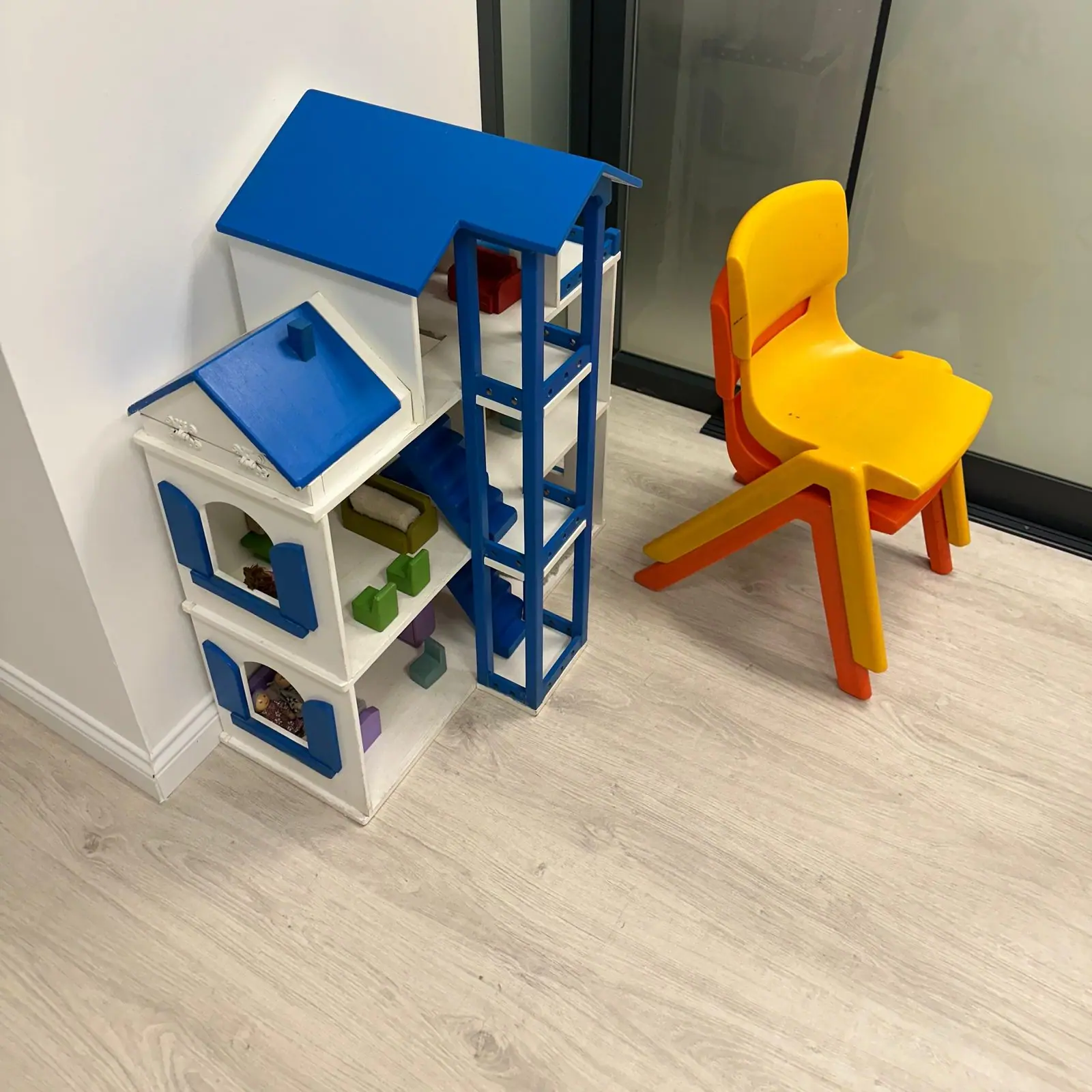 Oyun terapisi odasında mavi çatılı ahşap oyun evi ve sarı çocuk sandalyesi